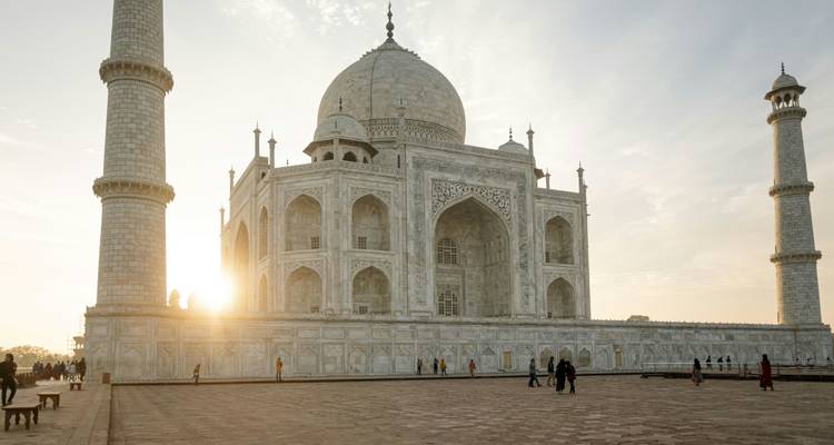 Early morning sunlight streams behind the Taj Mahal as visitors walk the marble courtyard.