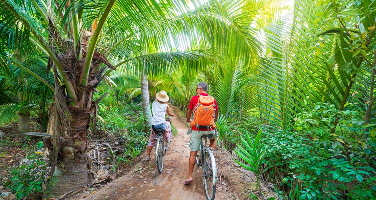 Couple bicycling on a lush green path.