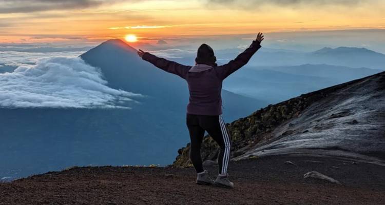 Person standing on a mountain summit at sunrise.
