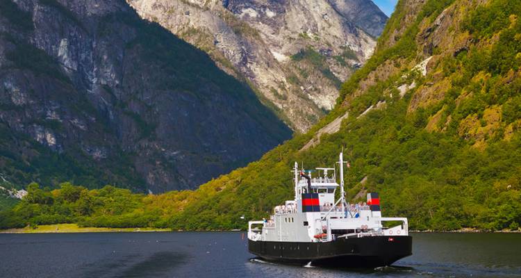 Ferry dans un fjord entouré de montagnes escarpées et de verdure.
