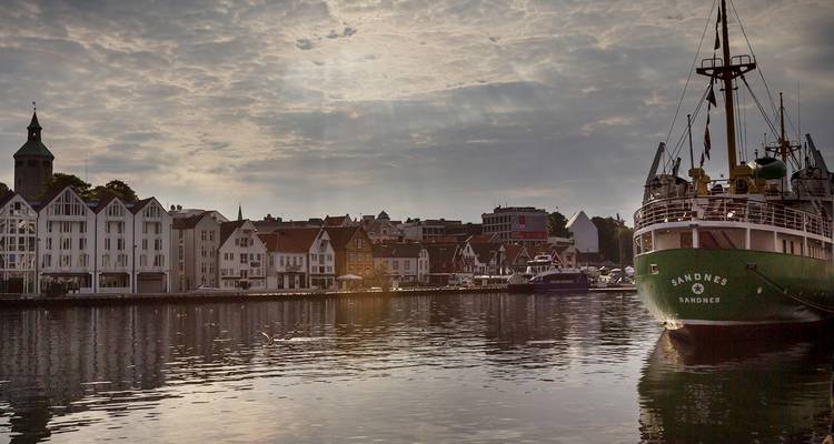 Front de mer historique en bois de Stavanger reflété dans un port calme à côté d'un navire vert vintage.