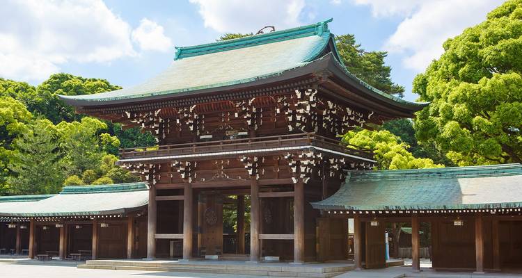Elegant houten torii-stijl hoofdpoort van een Shinto-heiligdom omgeven door weelderige groene bomen onder heldere hemel.