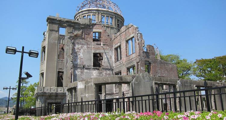 De Atomic Bomb Dome wordt omlijst door bloemen en een helderblauwe Hiroshima-lucht.
