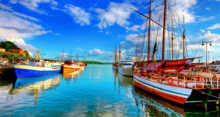 Barcos de madera y acero de colores amarrados en un puerto nórdico brillante bajo cielos azules vibrantes