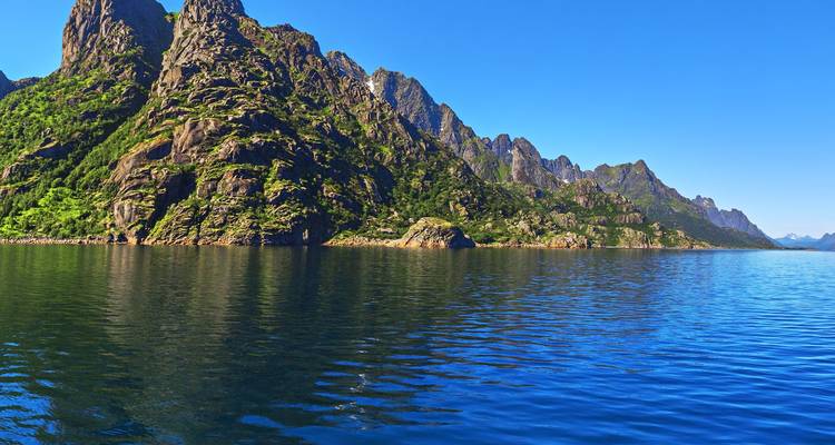 Uitgestrekt gebied van diepblauwe fjordwater met groene, rotsachtige bergwanden die zich in de verte uitstrekken onder een heldere hemel.