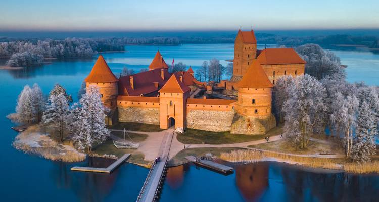 Fairytale Trakai Island Castle surrounded by frozen lake and frosted forest at dawn