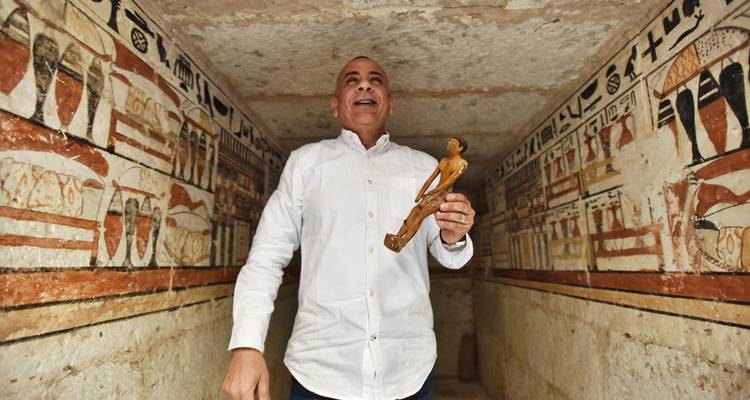 Une personne tenant une statuette dans une chambre aux murs hiéroglyphiques.