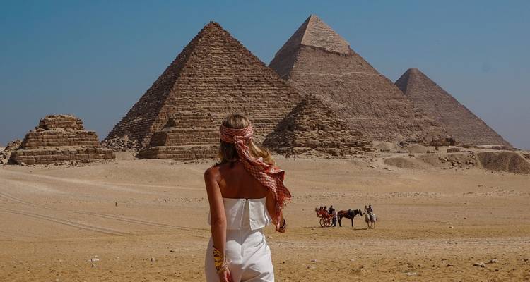 Femme debout devant les pyramides de Gizeh avec des chameaux en arrière-plan.