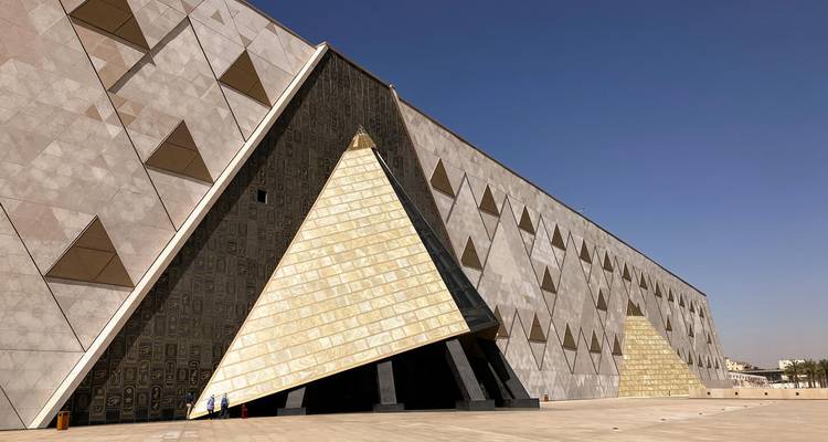 Facade d'inspiration pyramidale moderne du Grand Musée égyptien sous un ciel bleu dégagé.