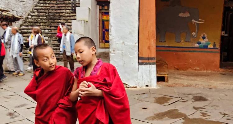 Two young monks in red robes walking and talking inside a monastery courtyard.
