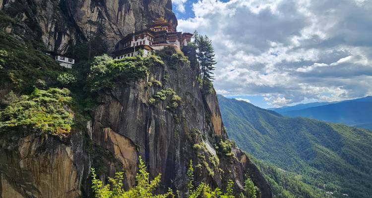 Iconic Tiger's Nest monastery perched on a sheer cliff above a lush Bhutanese valley under a dramatic sky.