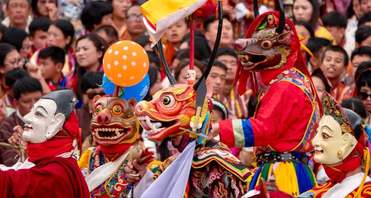 Masked dancers in vibrant costumes perform at a crowded Bhutanese festival.