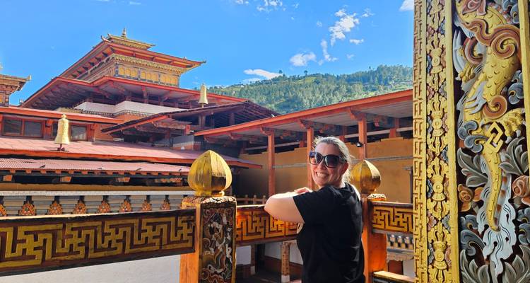 Smiling tourist poses inside an elaborately decorated Bhutanese monastery corridor.