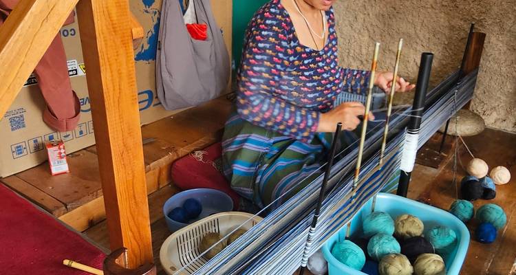 Bhutanese woman weaves textile on a traditional loom with colorful yarn balls.