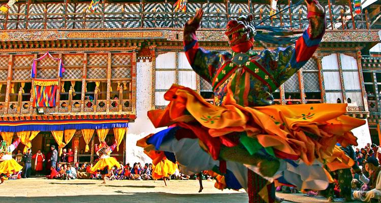 Danseur masqué tourbillonne en costume coloré lors d'un festival de monastère bhoutanais avec des spectateurs dans la cour.