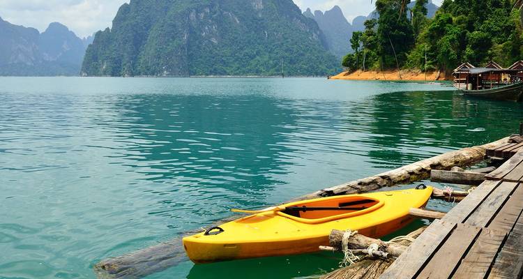 Bright yellow kayak tied to wooden pier on emerald lake surrounded by rainforest-covered limestone mountains