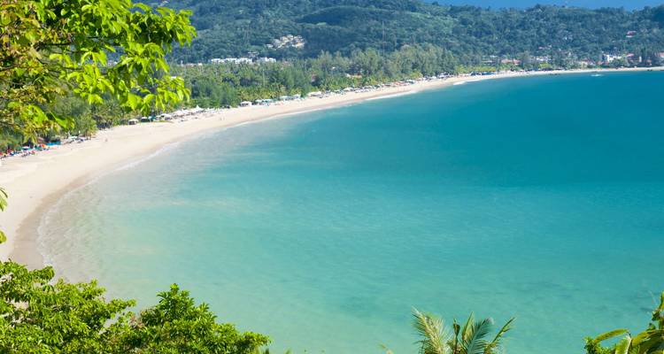 Aerial view of long curving tropical beach and turquoise bay backed by green hills