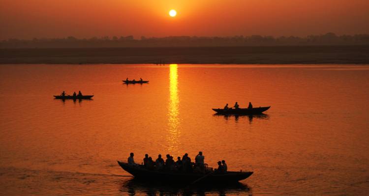 Des gens en bateau sur une rivière au coucher du soleil avec des reflets sur l'eau.