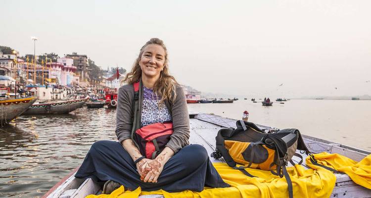 Femme assise sur un bateau, souriante devant un paysage urbain en arrière-plan.