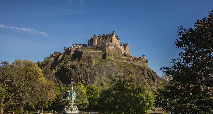 Château majestueux sur une colline avec une fontaine au premier plan.