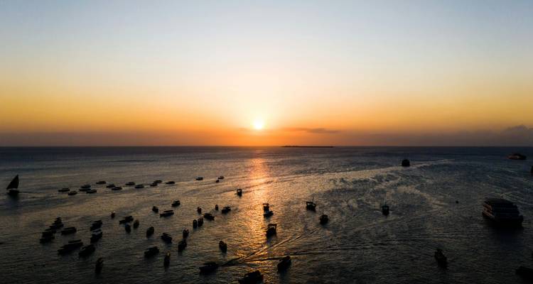 Coucher de soleil sur l'océan avec des bateaux et une ligne d'horizon en vue.