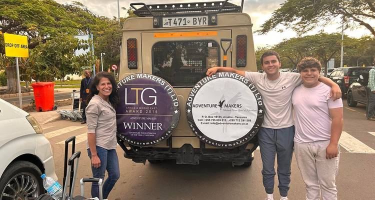 Une famille pose devant un véhicule avec des logos et des bagages à un aéroport.