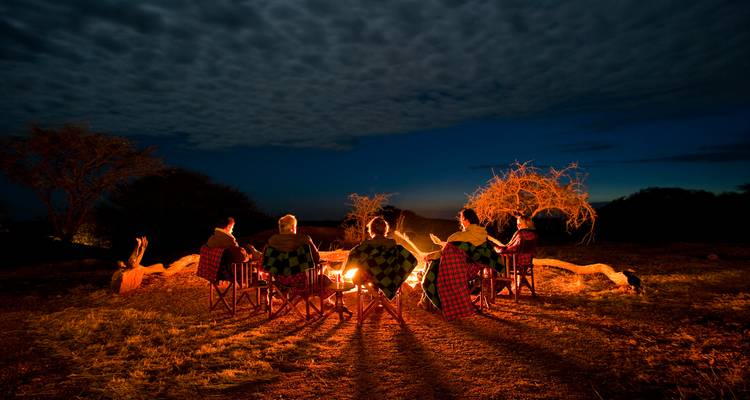 Un groupe de personnes assises autour d'un feu de camp sous un ciel étoilé.