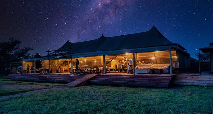 Un campement de tentes illuminé avec un ciel étoilé en arrière-plan.