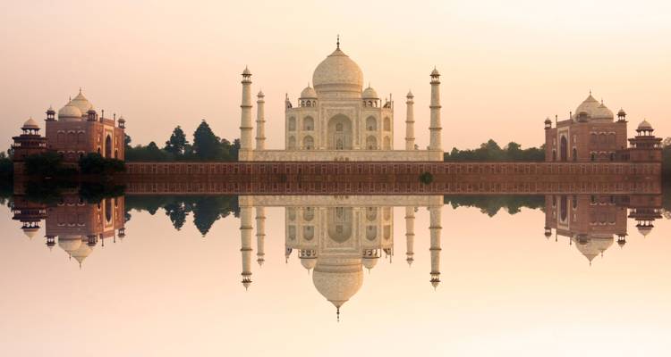 Taj Mahal mirrored in the calm water during sunrise.