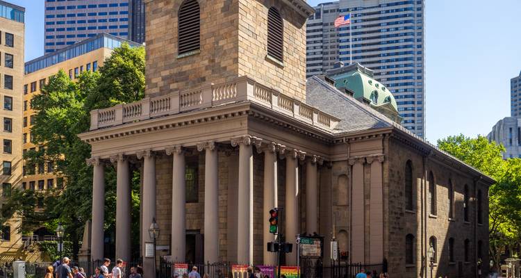 Une église en pierre historique avec des colonnes, entourée de bâtiments modernes.