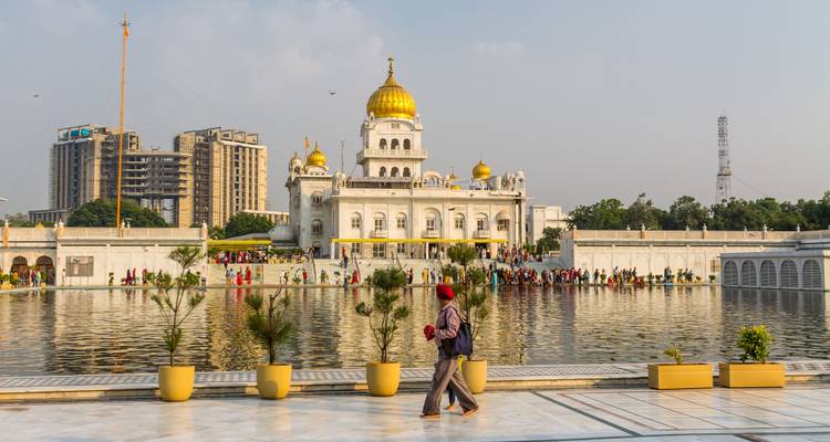 Templo sikh Gurdwara Bangla Sahib reflejado en su estanque sagrado mientras los visitantes caminan por el patio de mármol