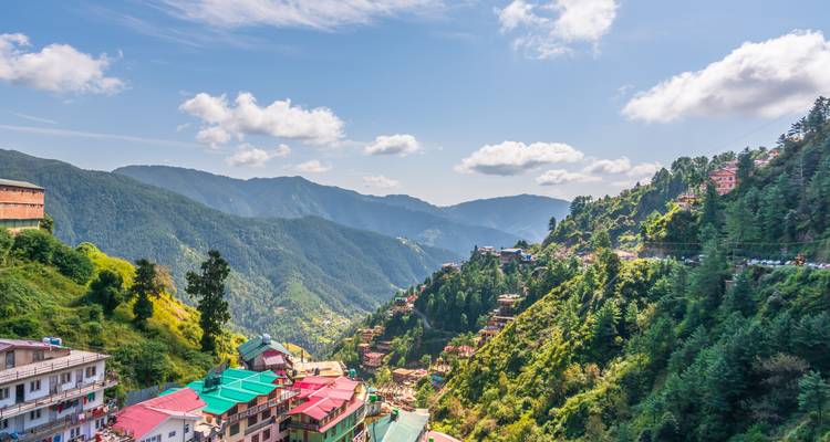 Felgekleurde daken van het stadje op de heuvel kijken uit over bosrijke dalen en verre Himalaya-bergketens onder een blauwe lucht