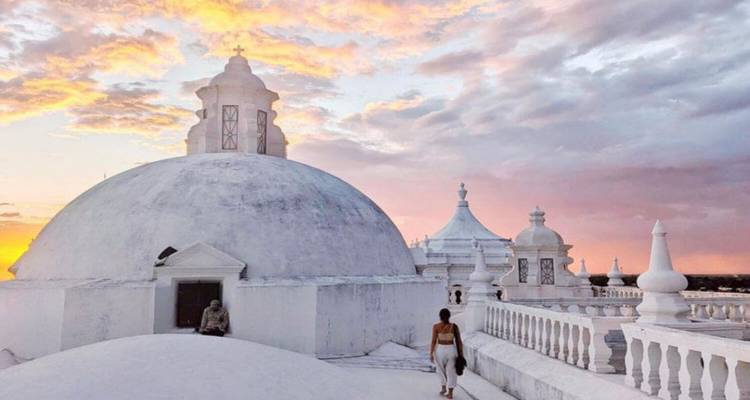 A woman walks on the rooftop of a white dome building at sunset.