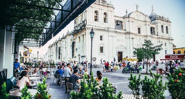 A lively plaza with people sitting and walking near a cathedral.
