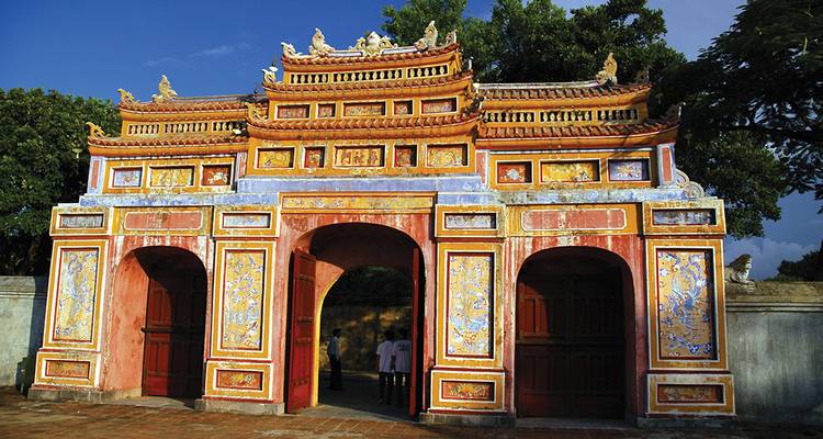 Ancienne porte rouge et dorée avec des motifs complexes et un ciel bleu.