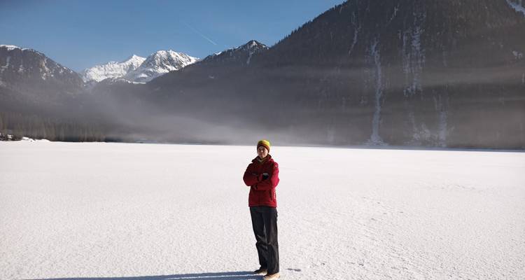 Personne debout sur un lac gelé avec des montagnes en arrière-plan.