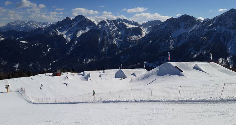 Zone de ski de montagne enneigée avec des rampes et des sommets au loin.