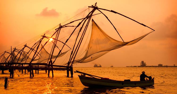 Vue de filets de pêche chinois au coucher du soleil avec un pêcheur dans un bateau.