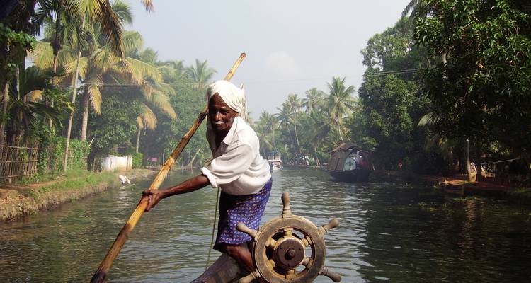 Un homme âgé ramant sur un bateau traditionnel sur un canal bordé de palmiers.