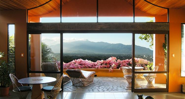 Stylish open lounge with wicker furniture framing a sweeping valley and mountain view beyond blooming bougainvillea.