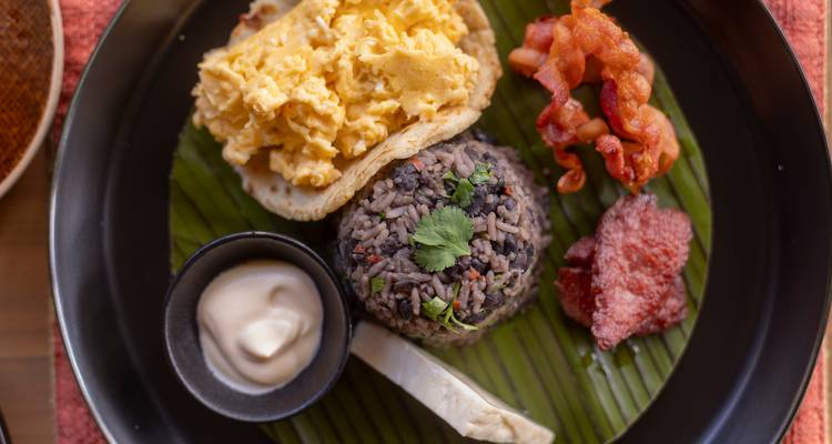 Traditional Costa Rican breakfast with gallo pinto, eggs, bacon and sauces served on a banana leaf plate.