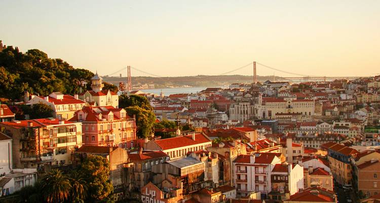 Panoramisch uitzicht tijdens het gouden uur over de daken van Lissabon naar de Ponte 25 de Abril die de Taagmonde overspant.