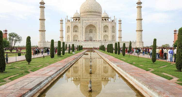 El icónico Taj Mahal de mármol blanco reflejado en su estanque central con visitantes alineados a lo largo del camino.