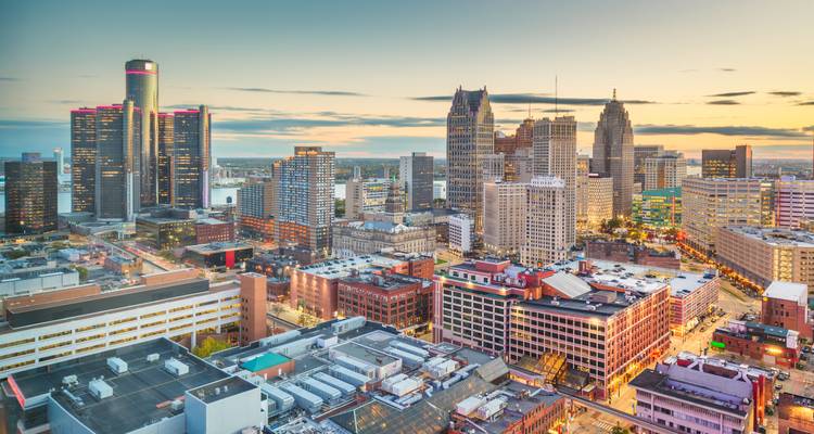 Detroit downtown skyline at dusk with warm lights reflecting off buildings and streets below