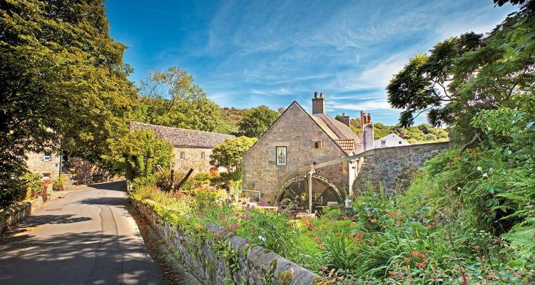 Quaint stone building by a bridge surrounded by greenery.