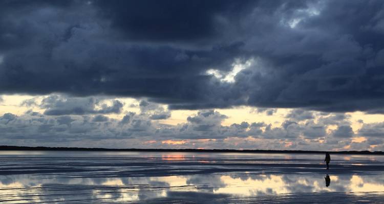 Dramatischer Himmel spiegelt sich bei Sonnenuntergang im Wasser wider