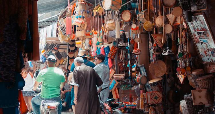 Un étal de marché animé avec divers produits traditionnels marocains et des gens qui font leurs courses.