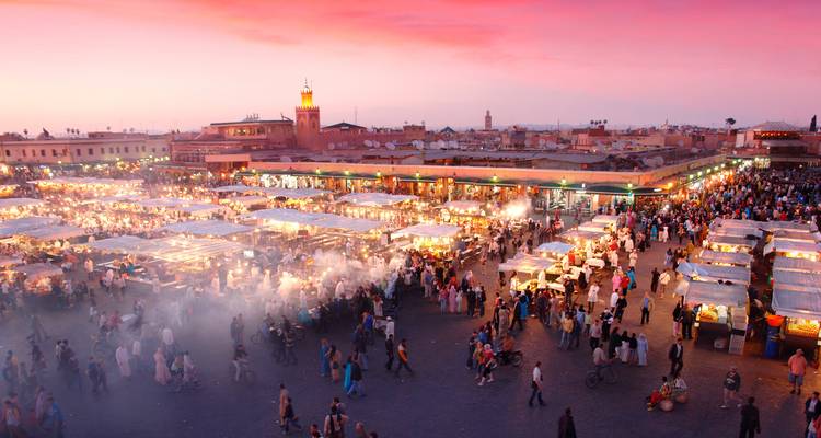 Un marché vibrant à Marrakech au coucher du soleil avec des lumières vives et beaucoup de monde.