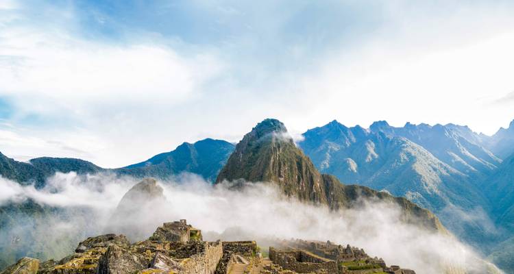 Machu Picchu with clouds covering parts of the ruins and mountains in the background.