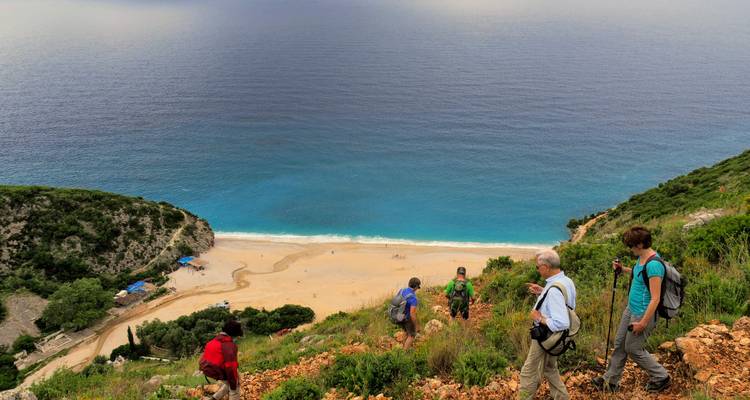 People hiking down a hill towards a beach.